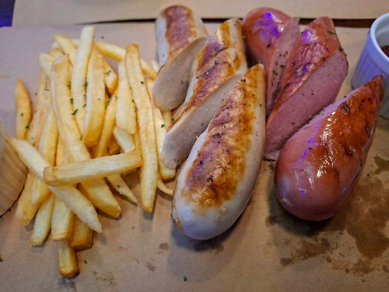 A platter of assorted sausages and fries, with various types of grilled sausages and golden French fries, served on brown paper.
