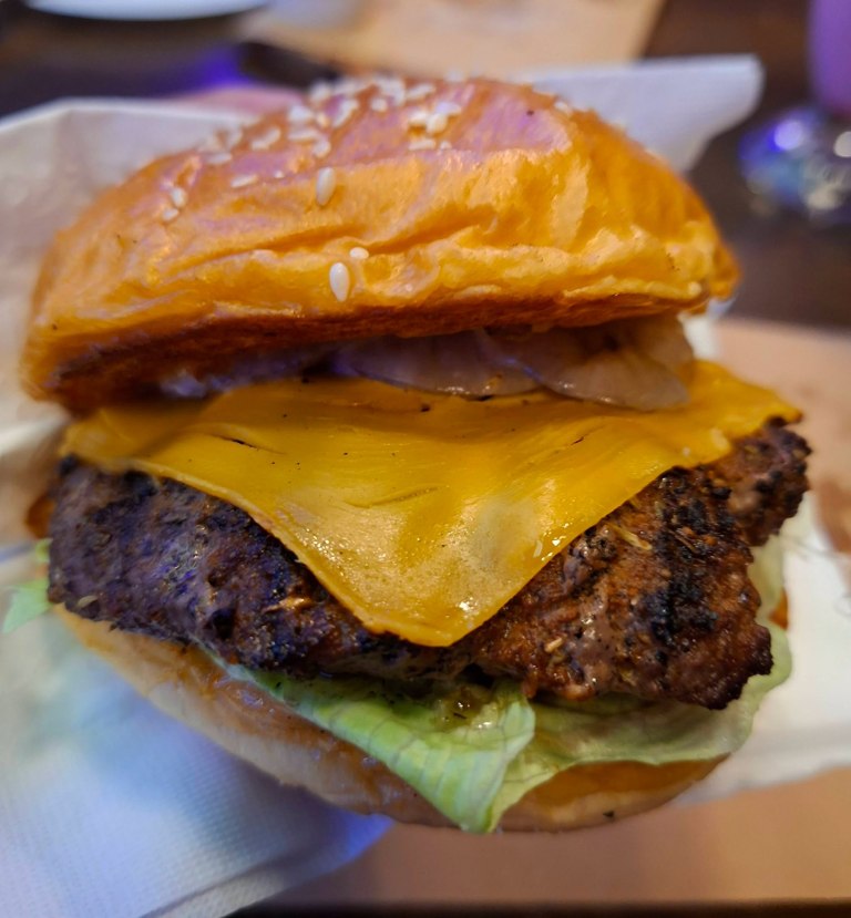 Close-up of a cheeseburger featuring a sesame seed bun, melted cheddar cheese, a beef patty, and lettuce.